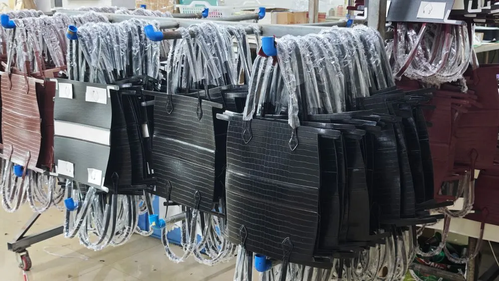 Stacks of structured handbag bodies and handles in black, brown, and burgundy tones neatly arranged on racks inside a production facility, highlighting the organized workflow of a custom made handbag factory.