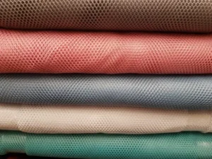 Stack of mesh fabrics in muted colors—brown, pink, blue, white, and teal—commonly used as breathable and lightweight handbag linings.