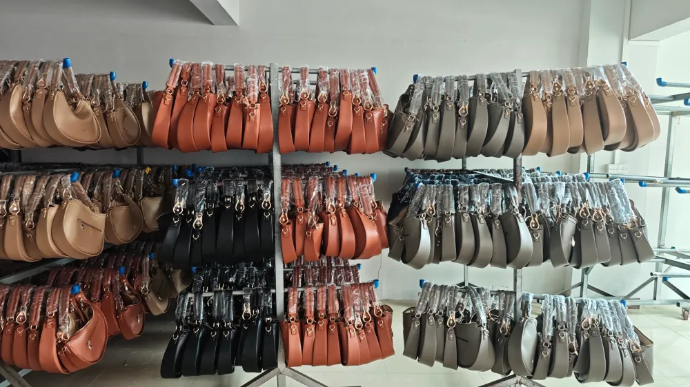 Multiple rows of finished leather handbags in various colors—tan, black, brown, and gray—neatly hung on metal racks inside a production facility, showcasing the organized output of a custom leather handbag manufacturer.