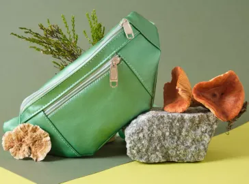 A green vegan leather handbag displayed with natural props like stones, mushrooms, and greenery, highlighting sustainability and eco-conscious fashion design.