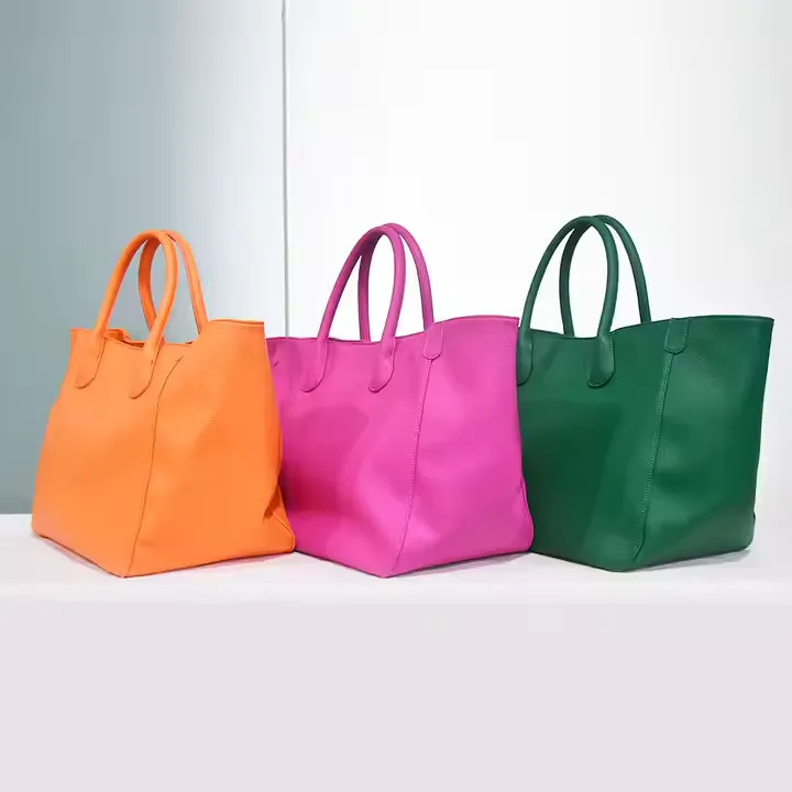 Three vibrant custom tote bags are displayed side by side in orange, magenta, and green colors. Each tote bag is made of textured leather with a structured, minimalist silhouette and dual top handles, ideal for daily use or shopping.
