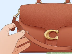 A close-up shot of a person's hand inspecting the leather strap and hardware of a brown Coach bag with a prominent gold "C" logo. The image highlights the texture of the leather and the quality of the metal, demonstrating key elements to check when learning how to tell if a Coach bag is real.