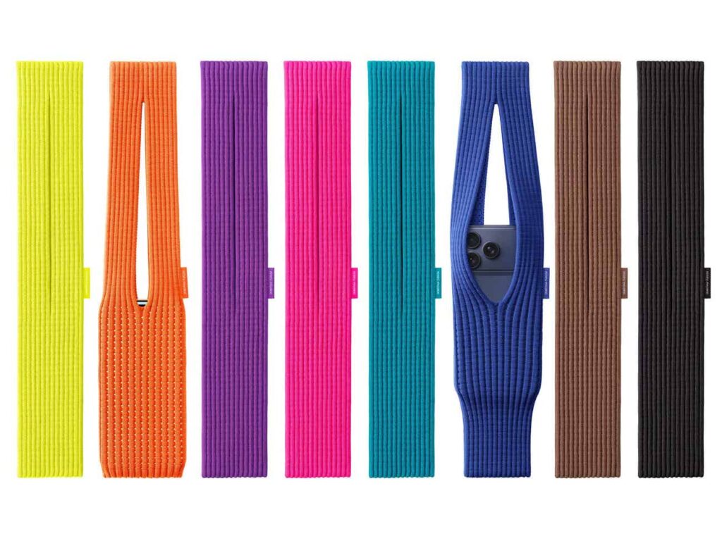 A product image displaying eight colorful, knitted phone slings (or sleeves) arranged vertically in a row against a white background. The colors from left to right are: neon yellow, bright orange, purple, hot pink, teal, royal blue, brown, and black. Each item features a ribbed knit texture. The sixth sling, in royal blue, is shown holding a smartphone, with a cutout revealing the phone's camera lenses.